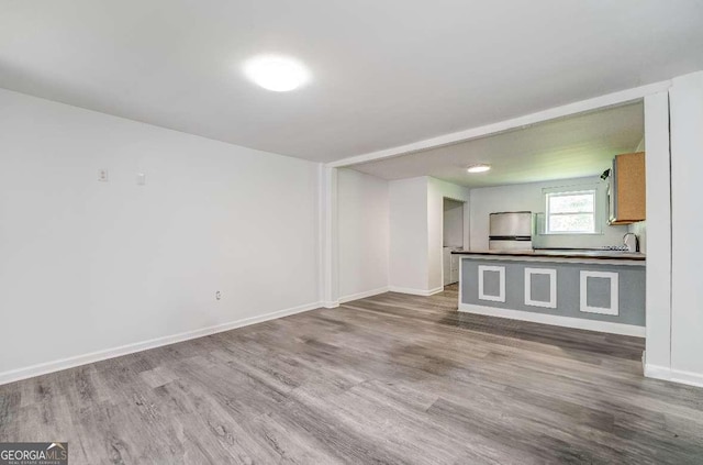 unfurnished living room with a sink, baseboards, and wood finished floors