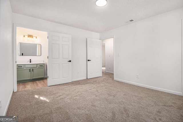 unfurnished bedroom featuring light carpet, ensuite bath, visible vents, and baseboards