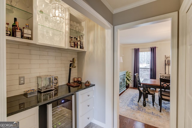 bar featuring tasteful backsplash, ornamental molding, a bar, wood finished floors, and beverage cooler