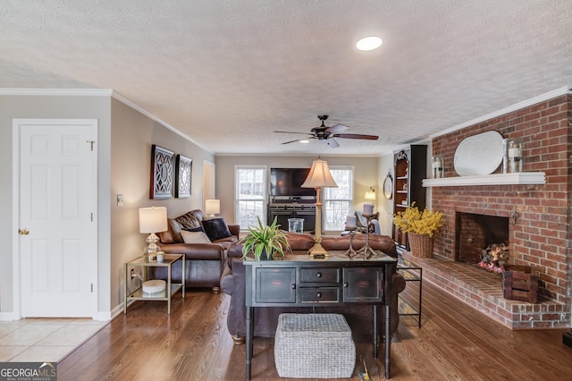 living area featuring a brick fireplace, crown molding, a textured ceiling, and wood finished floors