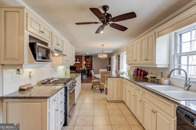 kitchen with light tile patterned floors, cream cabinets, appliances with stainless steel finishes, a sink, and under cabinet range hood