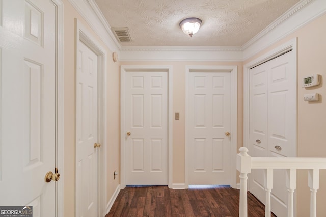 corridor featuring a textured ceiling, visible vents, baseboards, dark wood finished floors, and crown molding