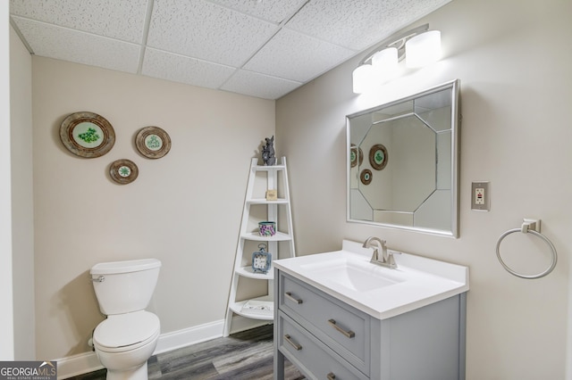 bathroom with a paneled ceiling, toilet, vanity, wood finished floors, and baseboards