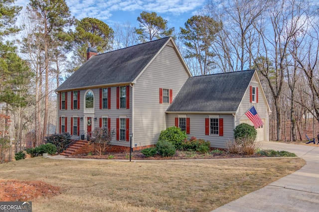 view of front of house featuring a shingled roof, a chimney, and a front lawn