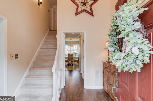 foyer entrance featuring dark wood-style floors, baseboards, stairway, and visible vents