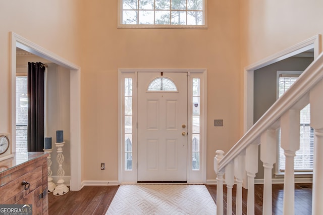 foyer with dark wood-style flooring, plenty of natural light, a towering ceiling, and baseboards