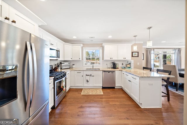 kitchen featuring a breakfast bar area, a peninsula, wood finished floors, visible vents, and appliances with stainless steel finishes