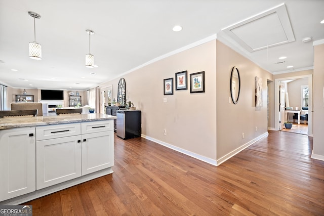 kitchen featuring light wood finished floors, open floor plan, decorative light fixtures, crown molding, and white cabinetry