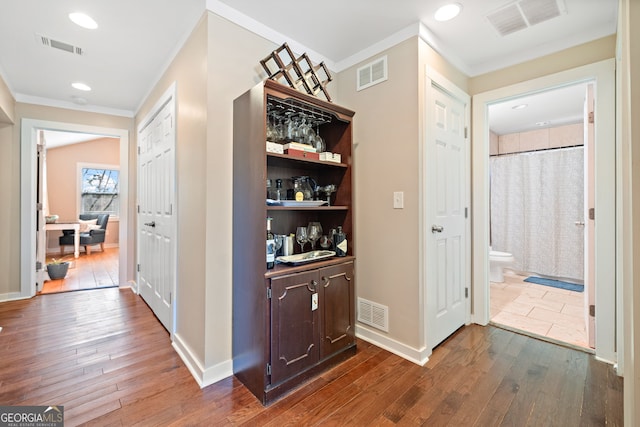 hallway featuring visible vents, dark wood finished floors, and ornamental molding