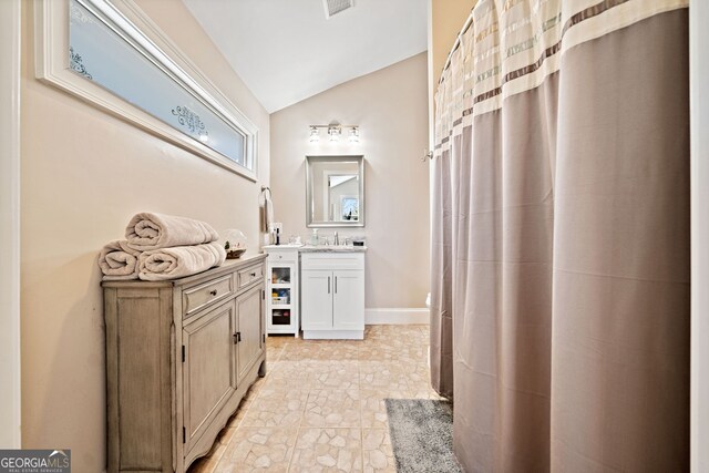 bathroom with vaulted ceiling, stone finish floor, vanity, and baseboards