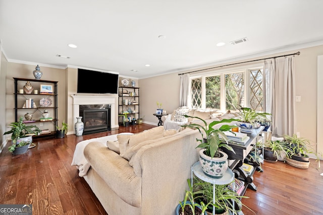 living room with a premium fireplace, visible vents, baseboards, ornamental molding, and hardwood / wood-style floors