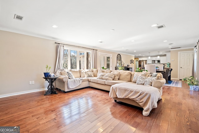 living area featuring visible vents, crown molding, and light wood-style flooring