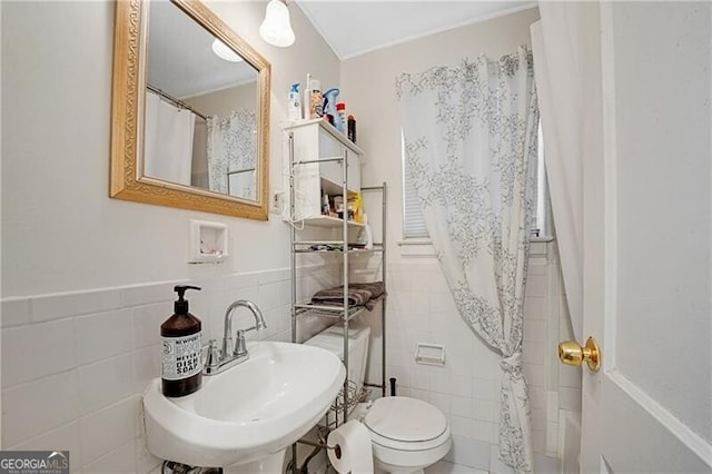 bathroom featuring toilet, wainscoting, a sink, and tile walls