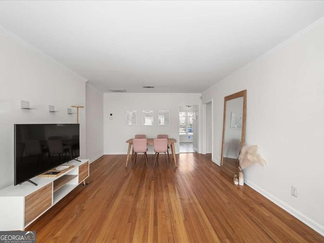 unfurnished living room with ornamental molding, visible vents, baseboards, and wood finished floors