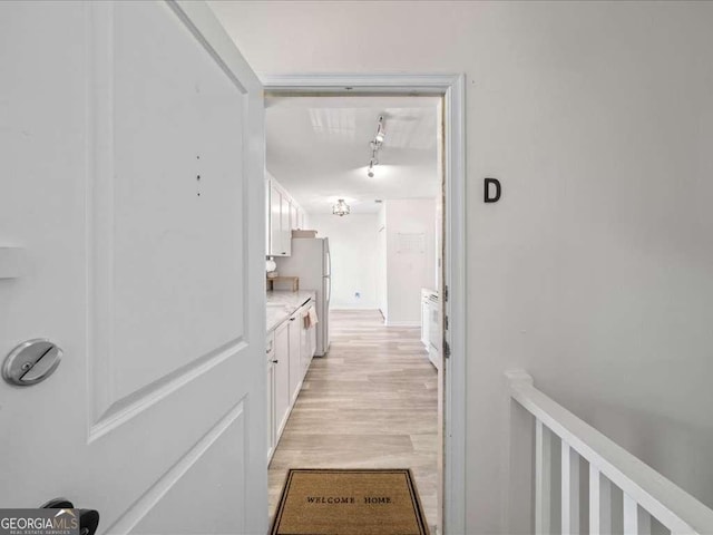 corridor with light wood finished floors and track lighting