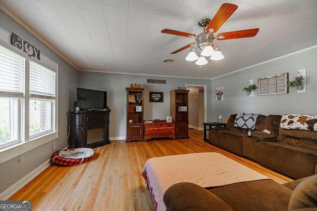 living area with light wood-type flooring, baseboards, ornamental molding, and a ceiling fan