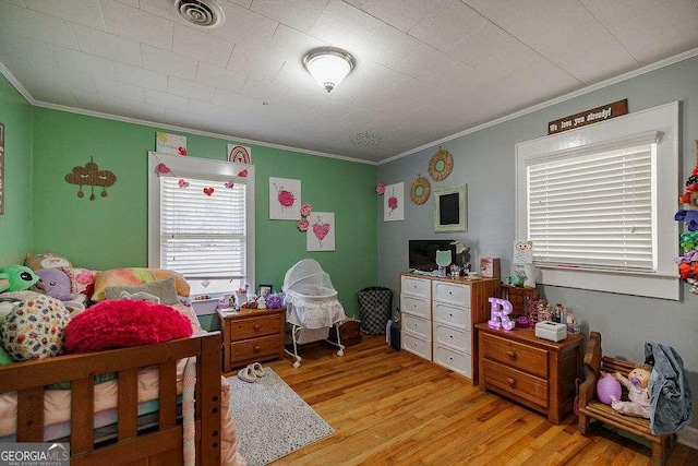 bedroom with light wood-style flooring, visible vents, and crown molding