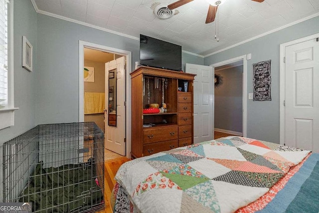 bedroom featuring a ceiling fan, visible vents, wood finished floors, and ornamental molding