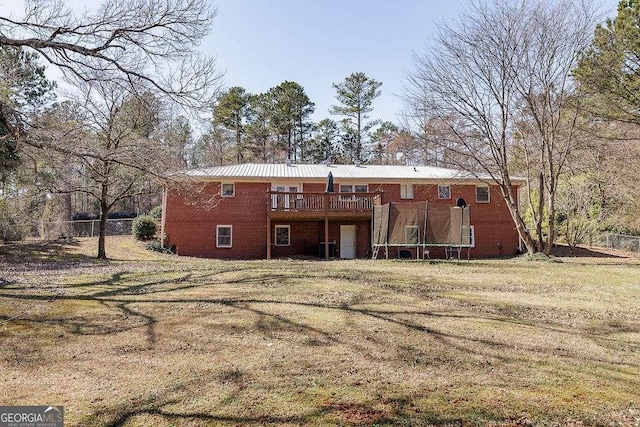 back of property with a deck, a yard, brick siding, and a trampoline