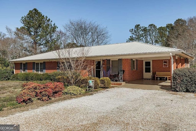 single story home featuring gravel driveway, brick siding, and metal roof