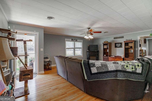 living area with visible vents, baseboards, a ceiling fan, ornamental molding, and light wood-type flooring