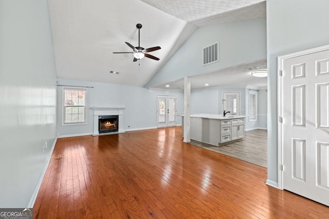 unfurnished living room with visible vents, a ceiling fan, light wood-style flooring, a sink, and a high end fireplace