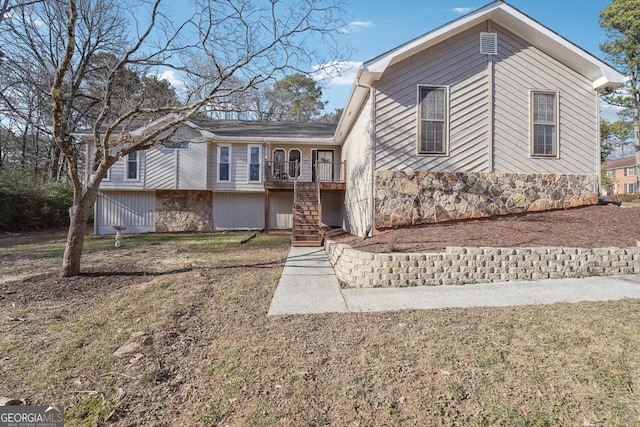 tri-level home featuring stone siding, stairway, and a front lawn