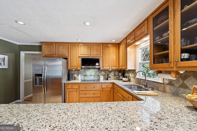 kitchen featuring appliances with stainless steel finishes, brown cabinetry, a sink, and glass insert cabinets