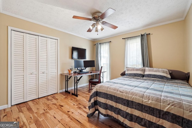 bedroom with light wood finished floors, baseboards, crown molding, a textured ceiling, and a closet