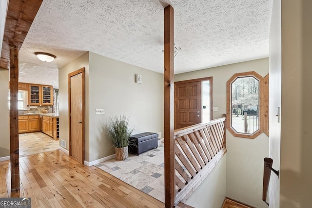 foyer with light wood-style floors, visible vents, a textured ceiling, and baseboards