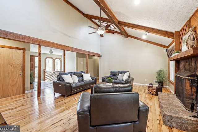 living area with high vaulted ceiling, a stone fireplace, light wood-style flooring, a ceiling fan, and beamed ceiling