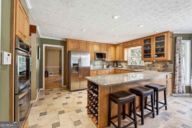 kitchen featuring light stone counters, appliances with stainless steel finishes, glass insert cabinets, a sink, and a kitchen breakfast bar