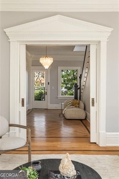 doorway with baseboards, ornamental molding, wood finished floors, stairs, and a chandelier