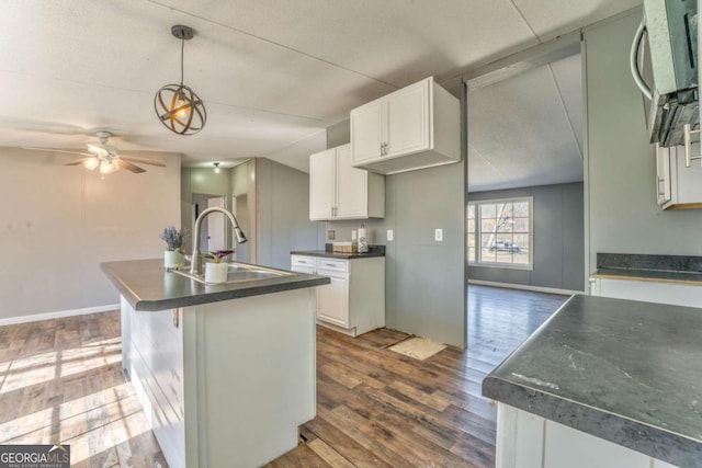 kitchen with a sink, white cabinetry, an island with sink, dark countertops, and decorative light fixtures