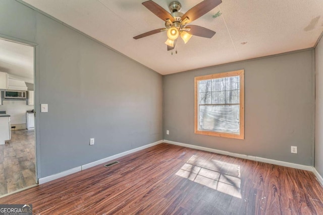 empty room with baseboards, visible vents, a ceiling fan, wood finished floors, and vaulted ceiling