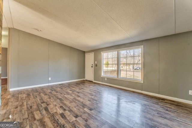 spare room featuring a textured ceiling, baseboards, and wood finished floors