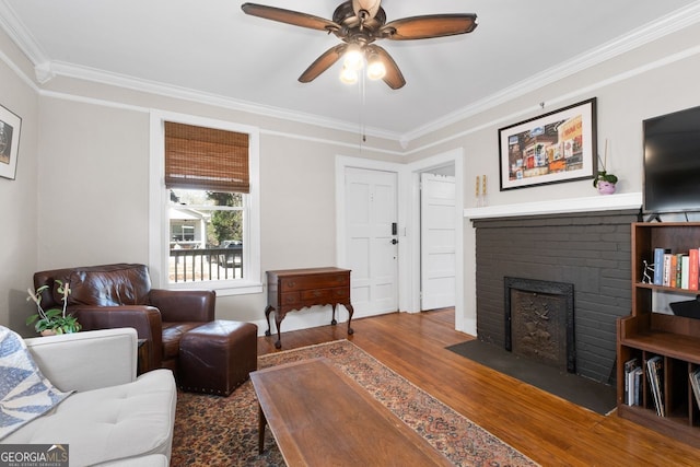 living room featuring ceiling fan, ornamental molding, a brick fireplace, and wood finished floors