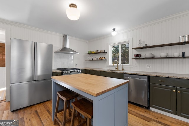 kitchen with wall chimney exhaust hood, butcher block counters, stainless steel appliances, open shelves, and a sink