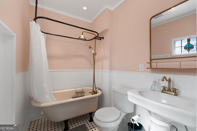 full bath featuring toilet, a wainscoted wall, crown molding, a freestanding bath, and a sink