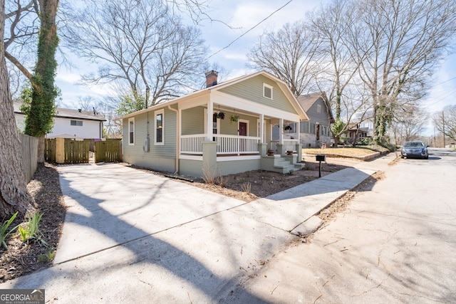 bungalow featuring driveway, a chimney, fence, and a porch