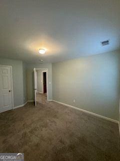 empty room with dark carpet, visible vents, and baseboards