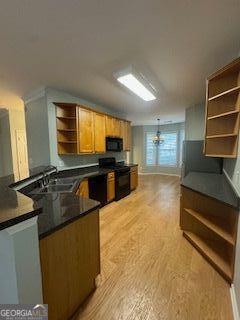 kitchen with light wood finished floors, open shelves, dark countertops, a sink, and black appliances