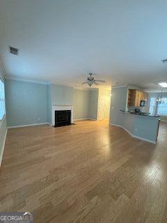 unfurnished living room with ceiling fan, wood finished floors, a fireplace with flush hearth, baseboards, and crown molding