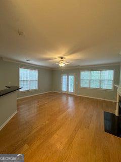 unfurnished living room with a fireplace, ornamental molding, a ceiling fan, wood finished floors, and baseboards