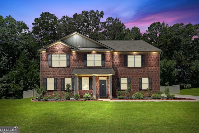 view of front of home featuring brick siding, board and batten siding, a front yard, and fence