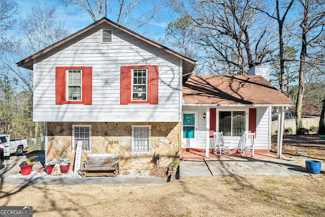 split level home with stone siding, a chimney, and fence