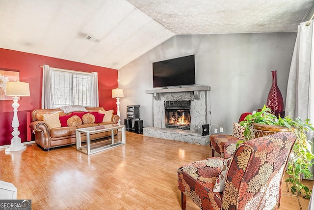 living room featuring visible vents, wood finished floors, vaulted ceiling, a textured ceiling, and a fireplace