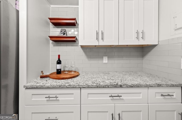 kitchen featuring decorative backsplash, freestanding refrigerator, light stone countertops, white cabinetry, and open shelves