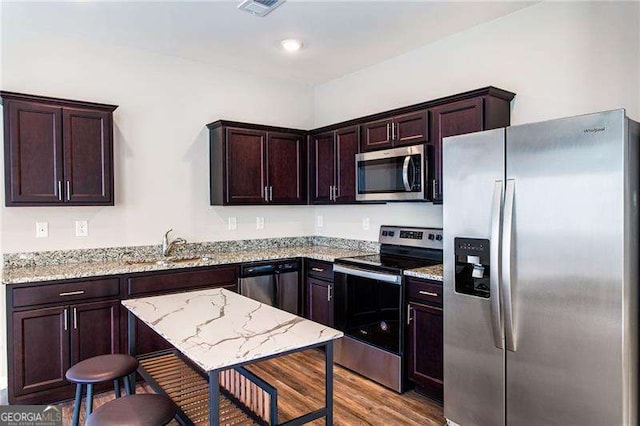 kitchen with stainless steel appliances, light stone countertops, visible vents, wood finished floors, and a kitchen breakfast bar