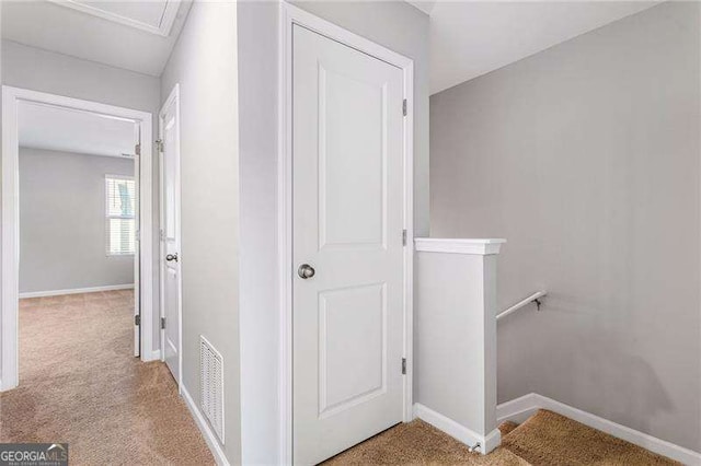 hallway featuring baseboards, visible vents, light carpet, and an upstairs landing